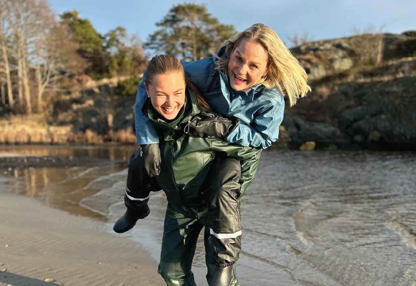 To damer smiler og ler på stranden kledd i storm foret regntøy fra hoppin