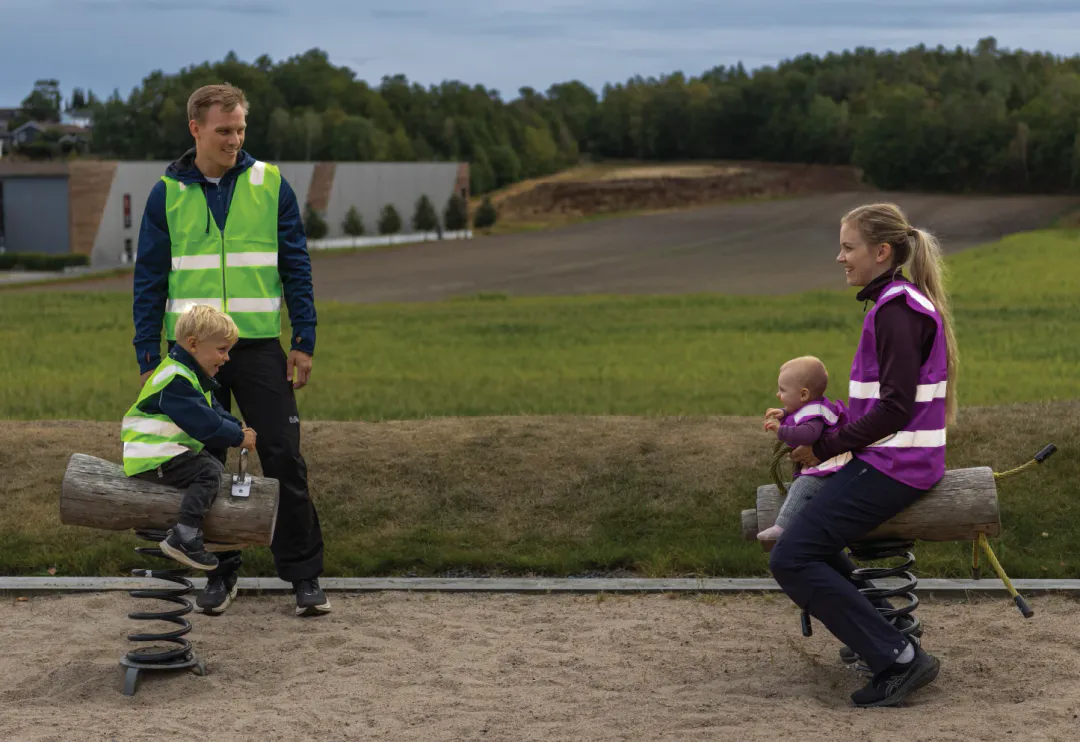 Barn og voksne sammen på lekeplass i matchende refleksvester fra hoppin
